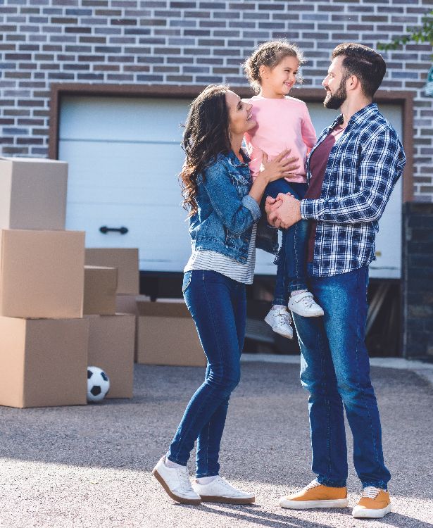 A happy couple holding their child in front of the house