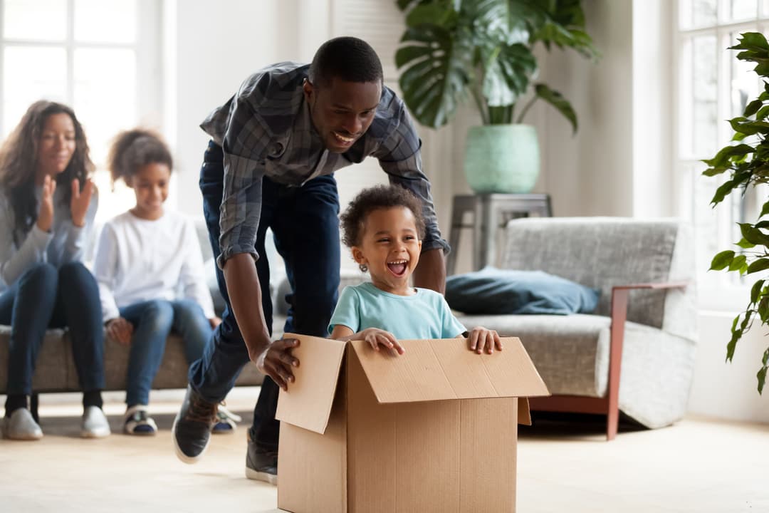 A man pushing his child in a box at their new home
