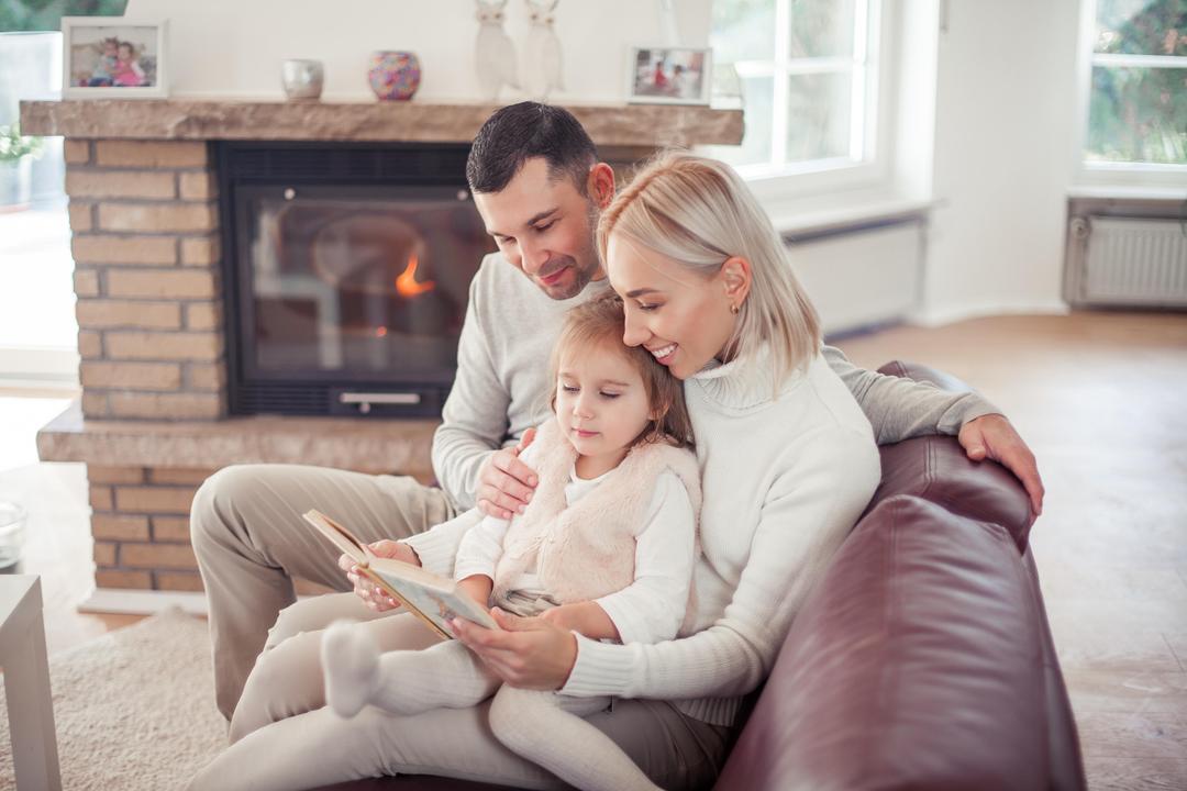 A couple reading a book to a child beside a fireplace
