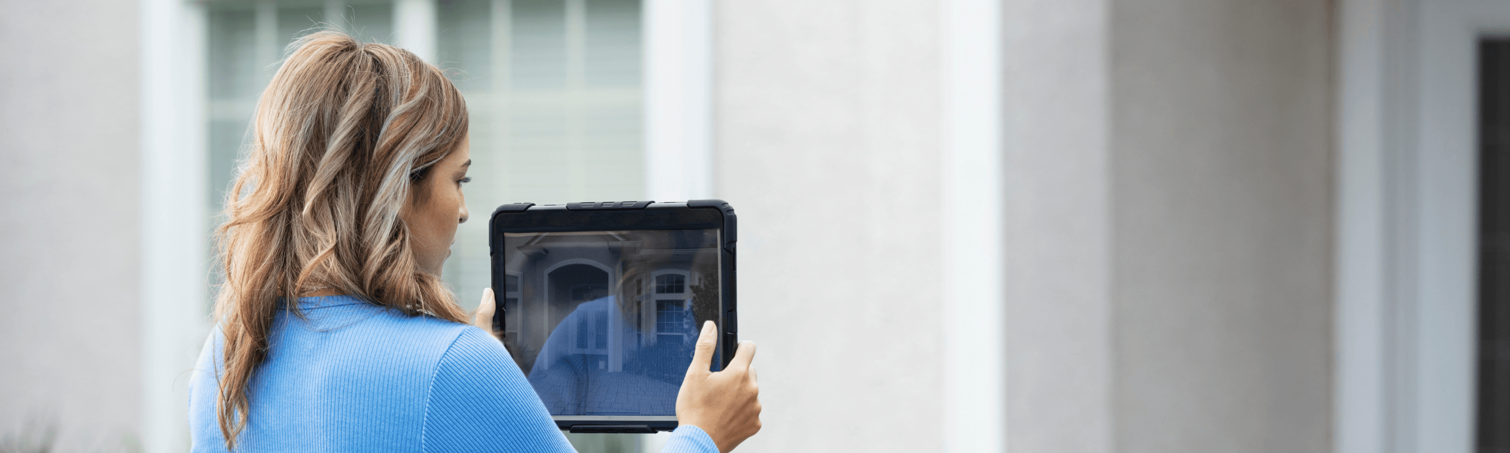 A person wearing holds a tablet, capturing an image of a house's entrance area outdoors.