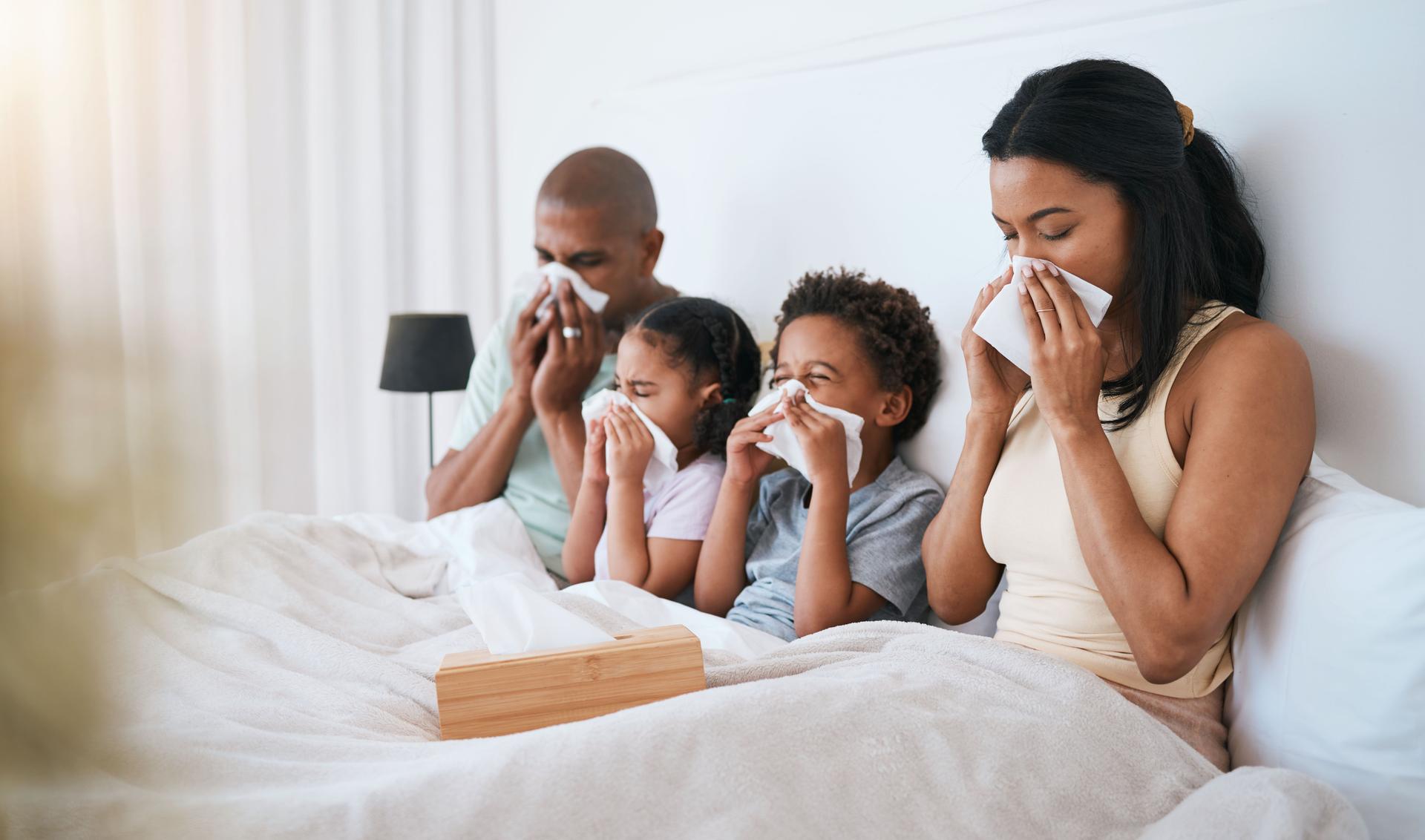 A family sitting in bed blowing their nose