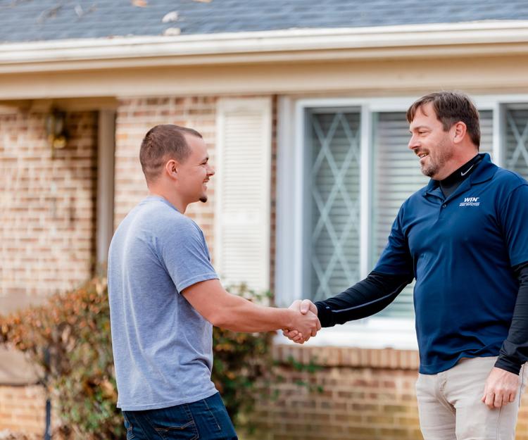 Homebuyer and WIN Home Inspector shaking hands outside a house.