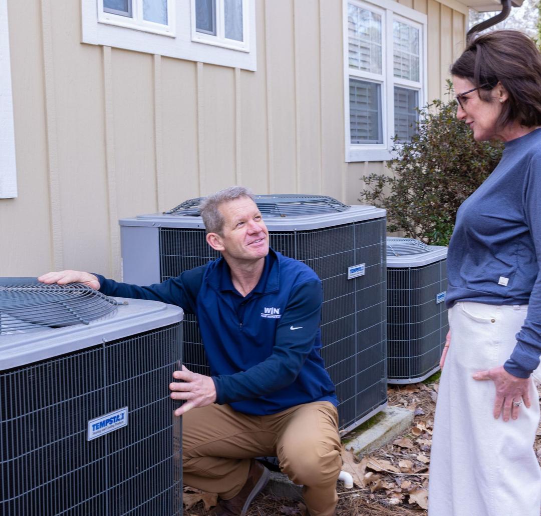 WIN Home Inspector looking at a heat pump outside the house