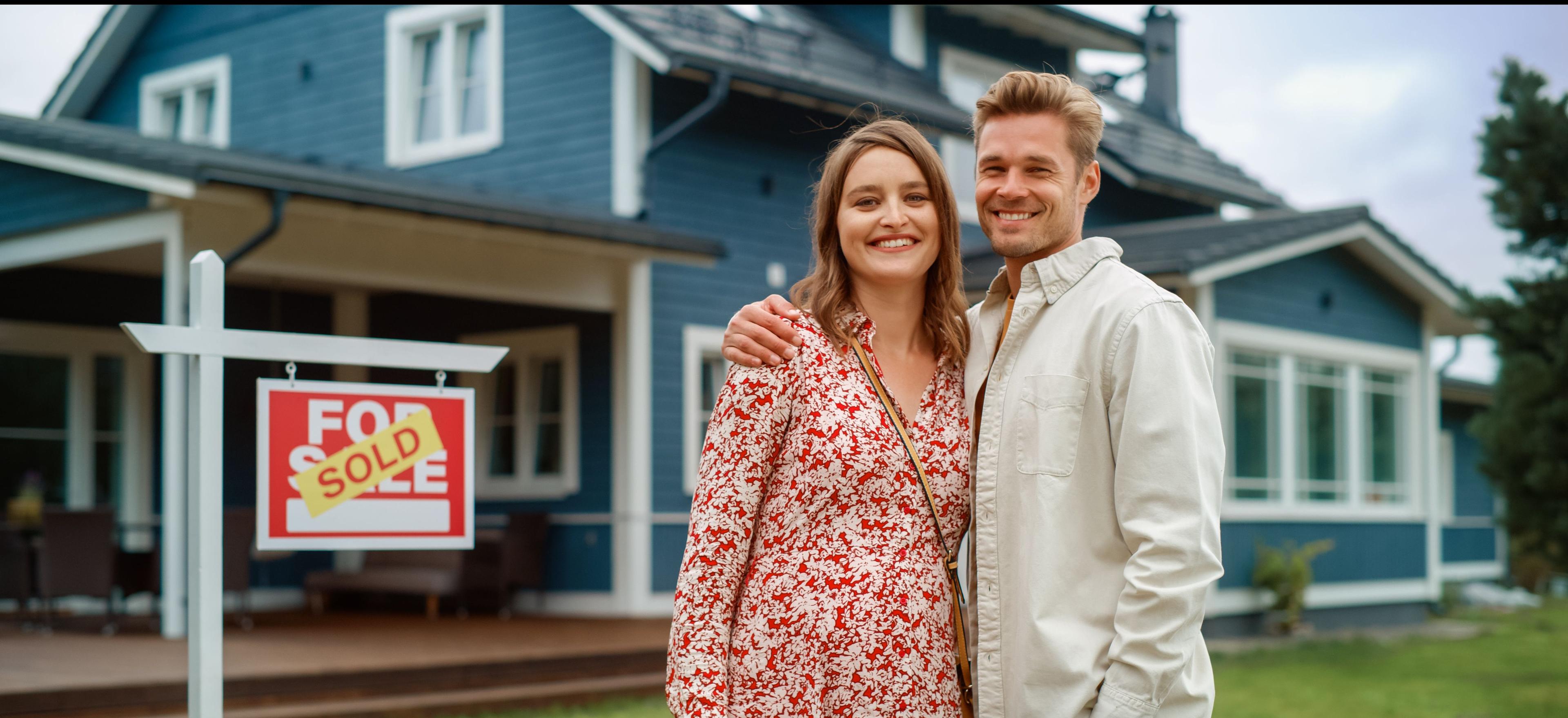 Smiling couple in front of a home sold sign board.