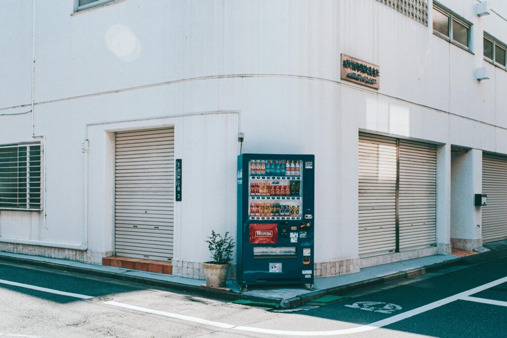 A quiet urban street corner featuring a vending machine against a white building.